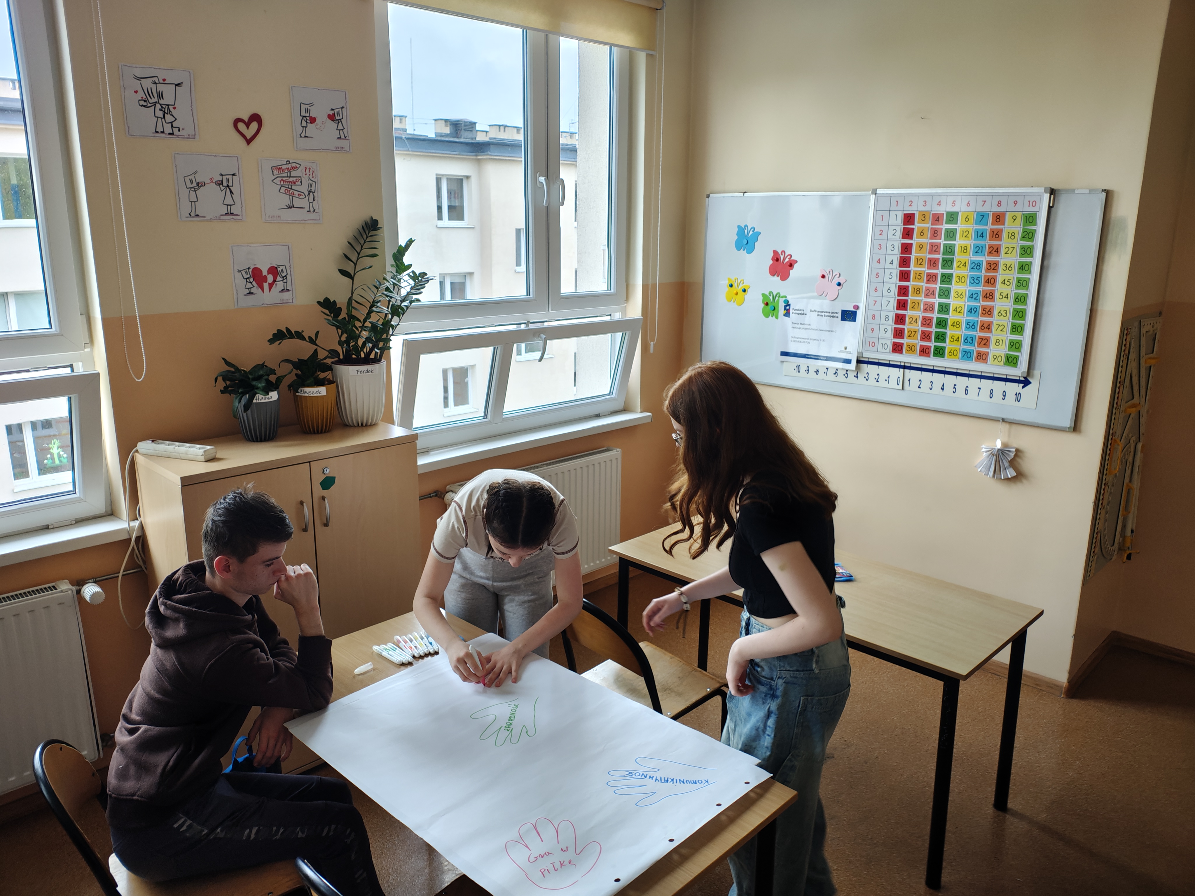 Zdjęcie przedstawia młodzież aktywnie uczestniczącą w zadaniu- opisywaniu swoich mocnych stron we wnętrzu dłoni, którą wszyscy uczniowie odrysowywali na płachcie papieru  