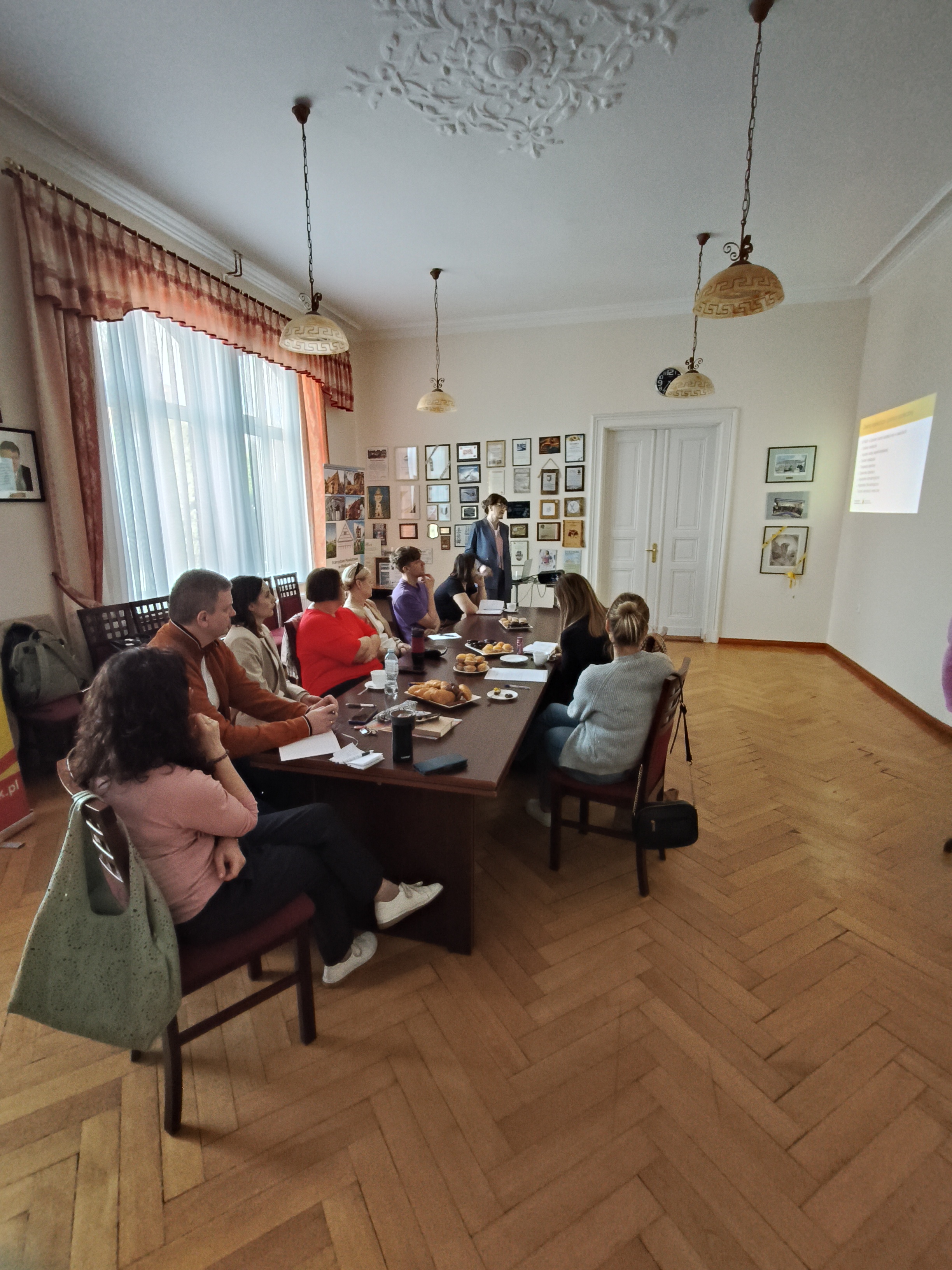 Zdjęcie prezentuje uczestników spotkania siedzących przy stole i słuchających wykładu przedstawicielki Pomorskiej Medycznej Szkoły Policealnej w Sztumie 